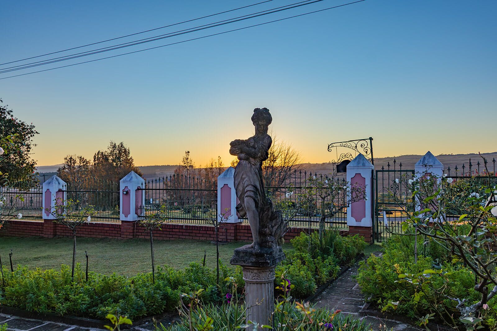 A garden with a statue, a fence, and a gate.
