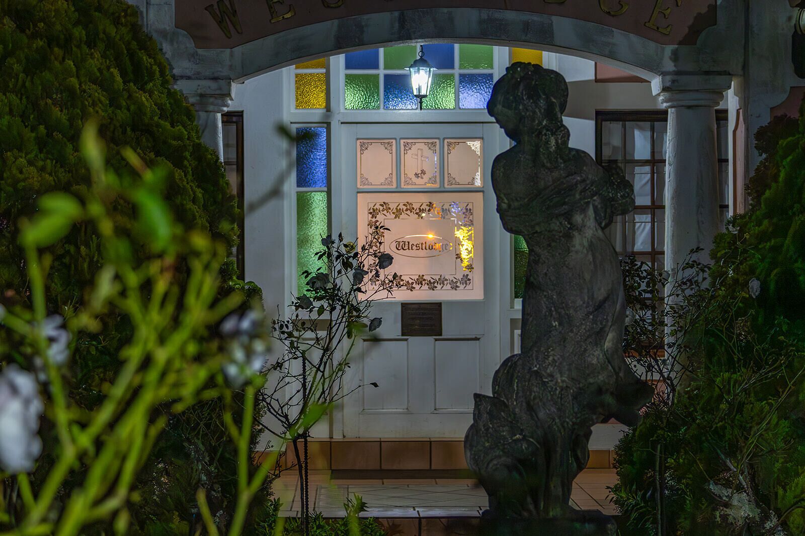 Una estatua en un jardín con un edificio al fondo, que presenta vidrieras y un letrero que dice 'Westminster'.