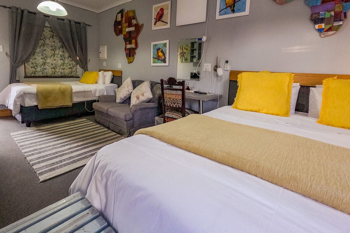 A hotel room with two beds, a sofa, a desk, and artwork on the walls.