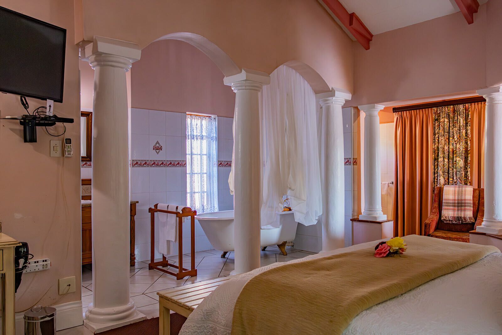 A bedroom with a large bed, a TV, and a bathroom with a bathtub and a shower.