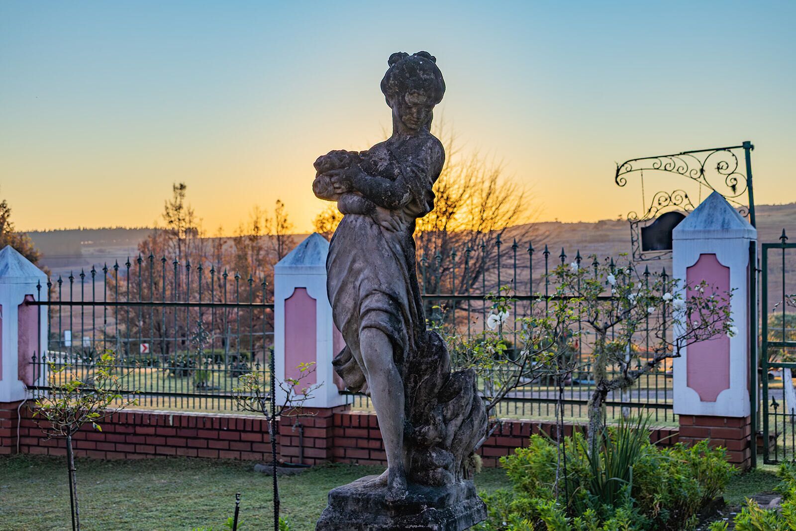 A statue in a garden with a fence and a gate in the background.
