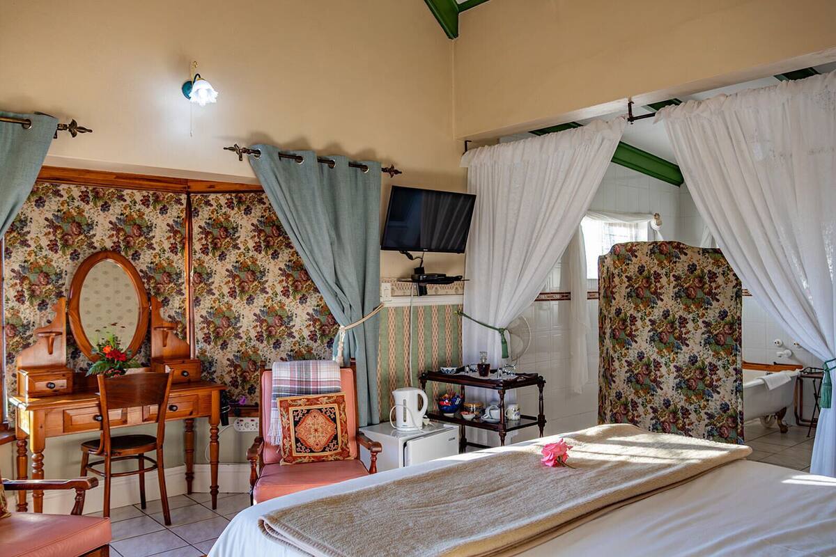 A bedroom with a bed, a desk, a chair, a mirror, a television, and curtains.