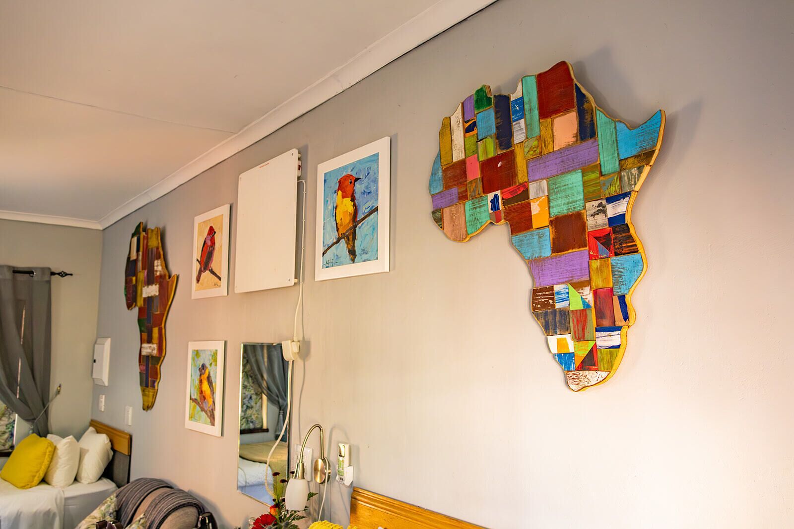 A hotel room with a bed, a large mirror, artwork on the wall, and a map of Africa.