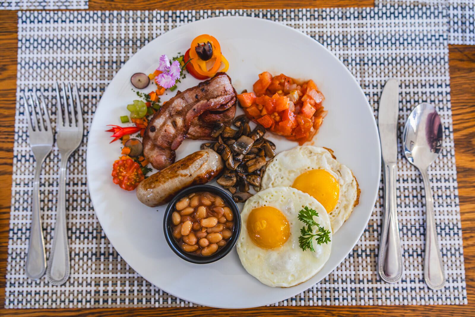 Un plato de comida para el desayuno con huevos, salchichas, frijoles y verduras.