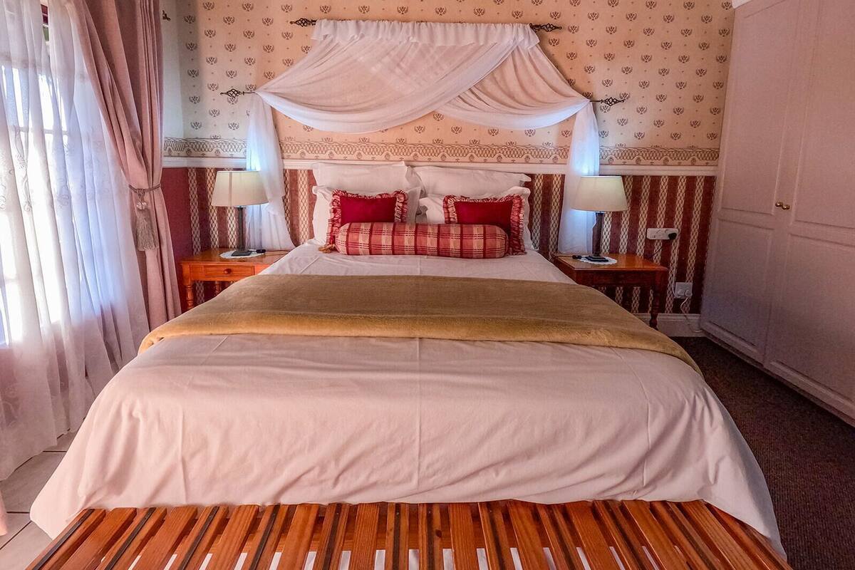 A bedroom with a canopy bed, striped wallpaper, and a wooden floor.