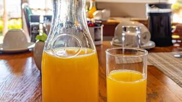A glass pitcher of orange juice with a flower on top, placed on a wooden table with a glass beside it.