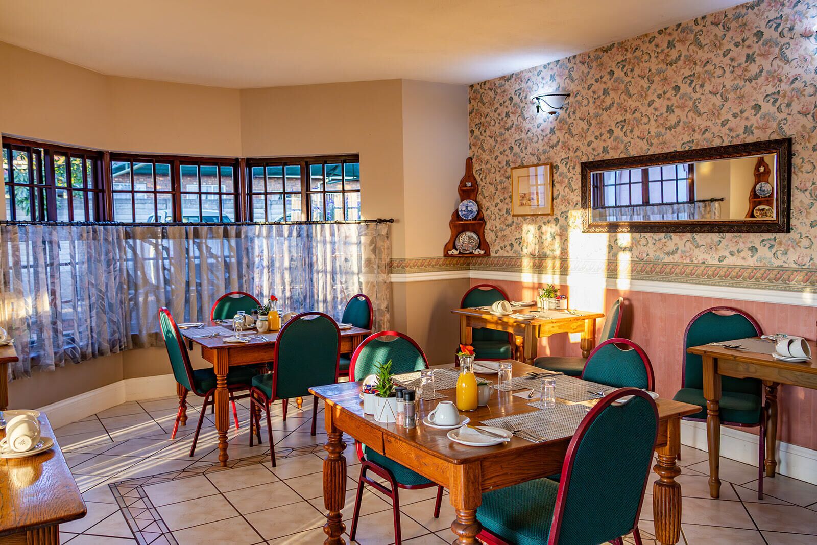 A dining area with a wooden table, green upholstered chairs, and a patterned wallpaper.