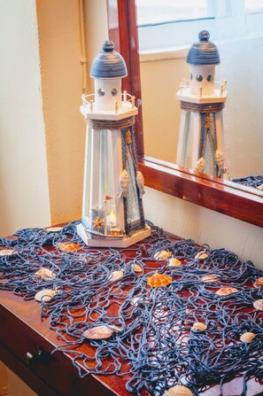 A wooden dresser with a nautical theme, featuring a small ship model, a lighthouse, and a net with seashells.