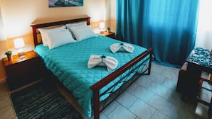 Une chambre d’hôtel bien rangée, avec un lit, des tables de chevet, une petite table et une fenêtre avec des rideaux.