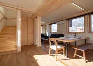 Un intérieur moderne avec un escalier en bois, un coin repas comprenant une table et des chaises, et un canapé en cuir noir en arrière-plan.