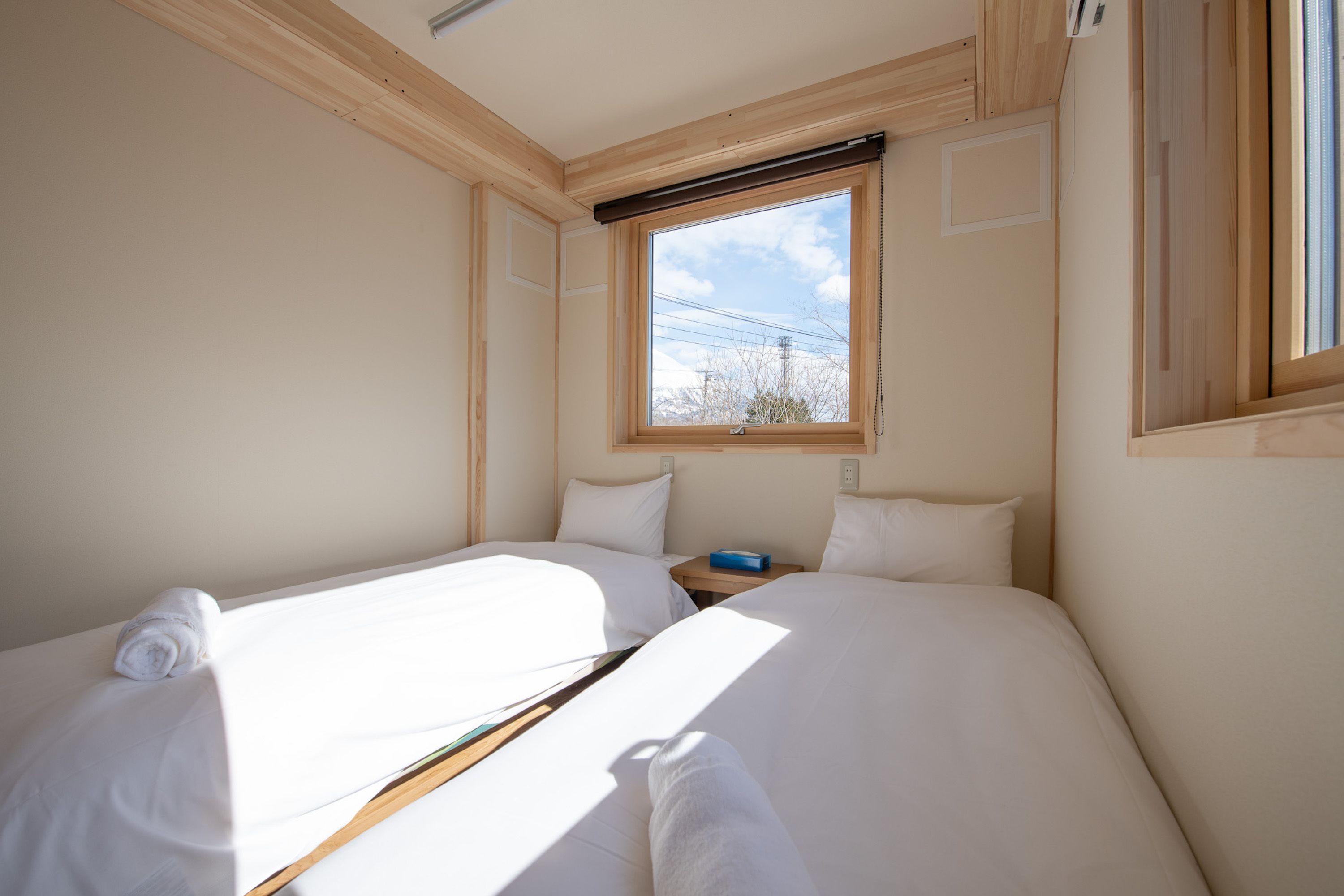 Ein Zimmer mit zwei Betten, Holzbalkendecke, einem Fenster mit Blick und einem blauen Gegenstand auf dem Nachttisch.