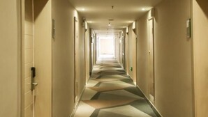 Ein langer, gut beleuchteter Hotelkorridor mit Türen auf beiden Seiten und einem gemusterten Teppich.