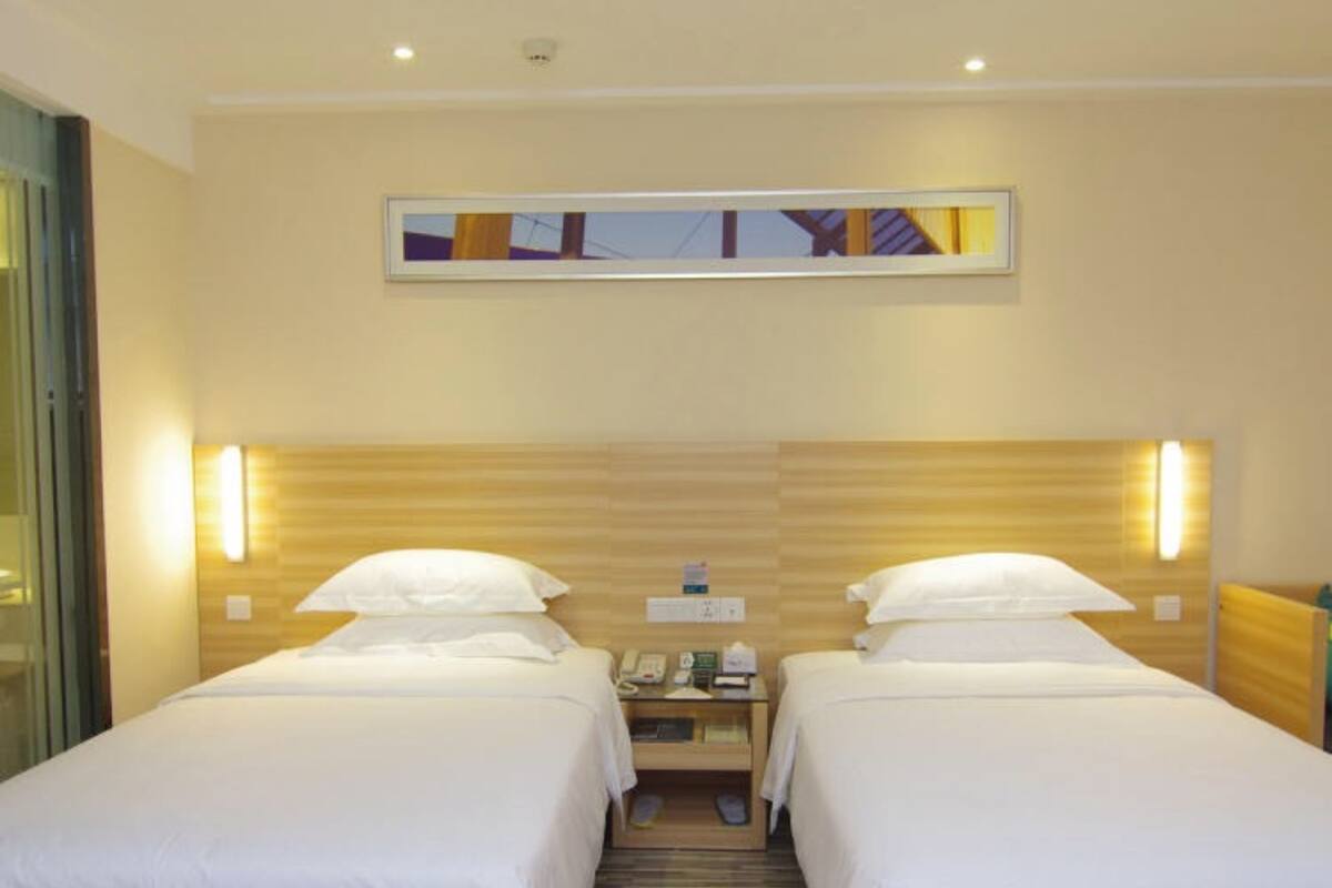 A hotel room with two single beds, a nightstand with a phone and a lamp, and a wooden headboard.