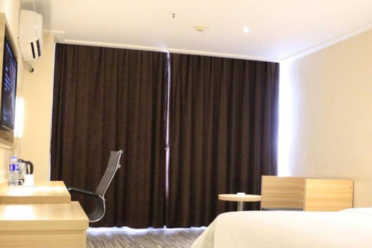 A hotel room with a bed, a desk, a chair, a small table, and a television.
