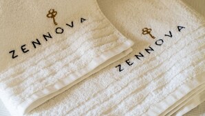 A stack of white towels with embroidered text and a key symbol. - Zennova 5 Antigonidon Sq (Thessaloniki)