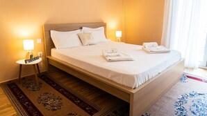 A neatly made bed with white linens and pillows, a small bedside table with a lamp, and a folded towel on the bed. - Zennova 5 Antigonidon Sq (Thessaloniki)