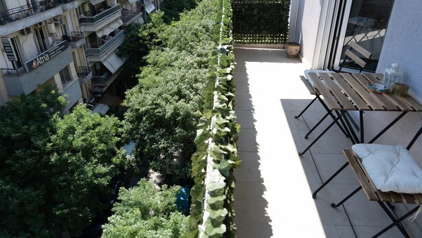A balcony with a wooden table and chairs, surrounded by lush greenery and a view of adjacent buildings. - Zennova 5 Antigonidon Sq (Thessaloniki)