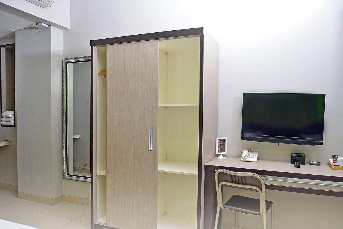 A hotel room with a desk, a TV, a chair, and a wardrobe.