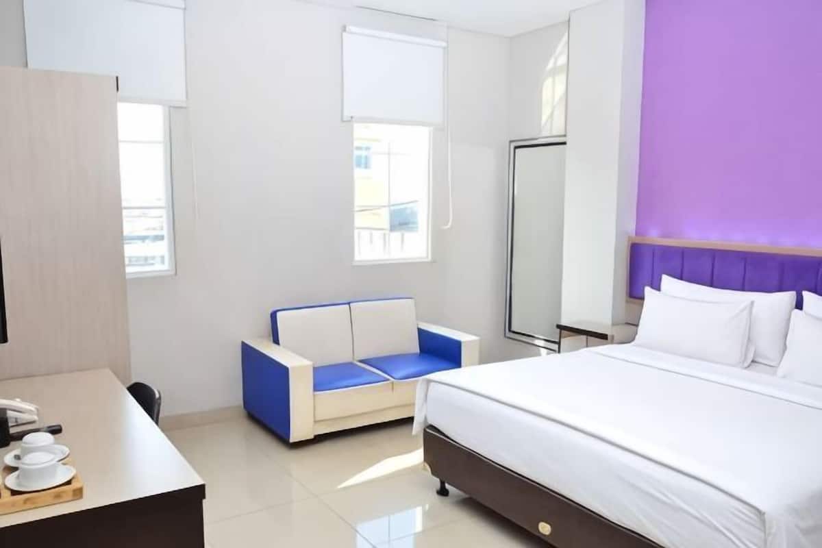 A hotel room with a bed, a desk, a chair, and a window.