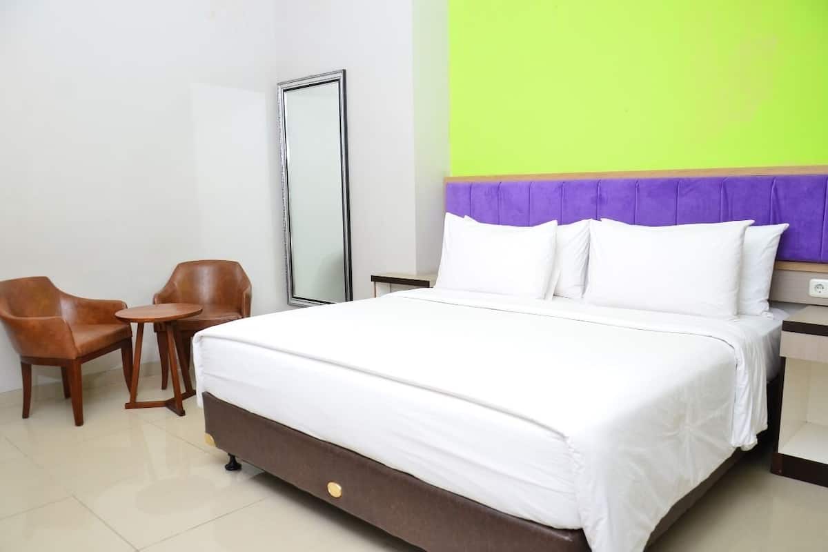 A hotel room with a bed, two chairs, a small table, a mirror, and a green wall.