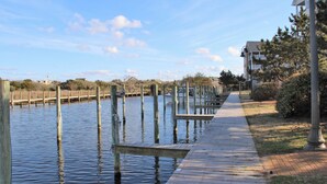 A wooden dock extending into calm water, surrounded by grassy areas and buildings. - SeaToo Waterfront Condo (Hatteras)