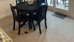 A dining area with a round table and four chairs, a ceiling fan, and a view of the deck through a glass door. - SeaToo Waterfront Condo (Hatteras)