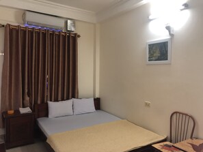 A bedroom with a bed, a nightstand, a chair, a wall-mounted air conditioner, and a painting. - Van Anh Motel (Hai Phong)