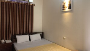 A hotel room with a bed, a nightstand, a lamp, a picture on the wall, and an air conditioning unit. - Van Anh Motel (Hai Phong)