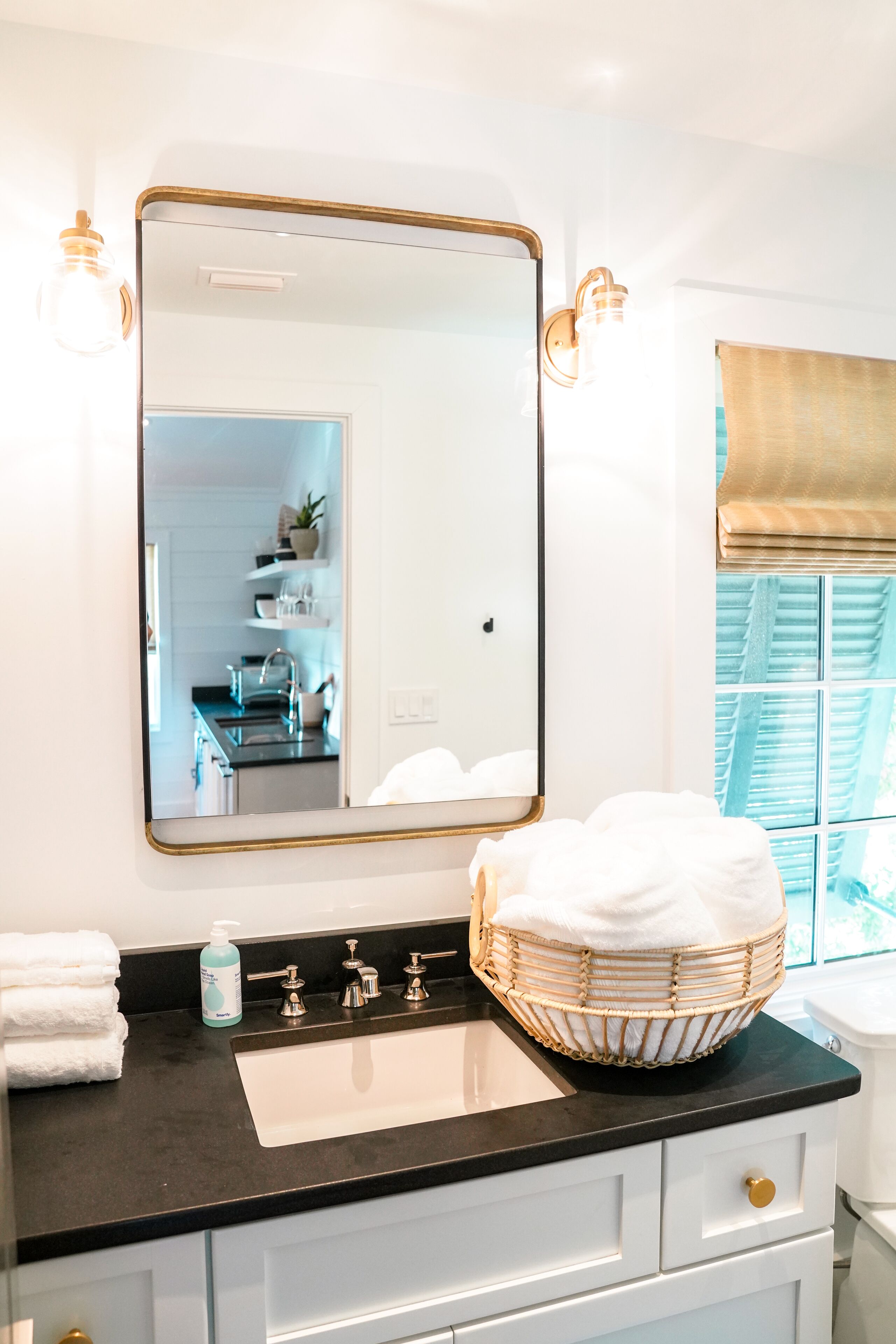 A bathroom with a large mirror, a black countertop, a white sink, and a wicker basket.