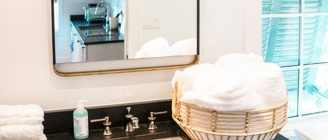 A bathroom with a large mirror, a black countertop, a white sink, and a wicker basket.