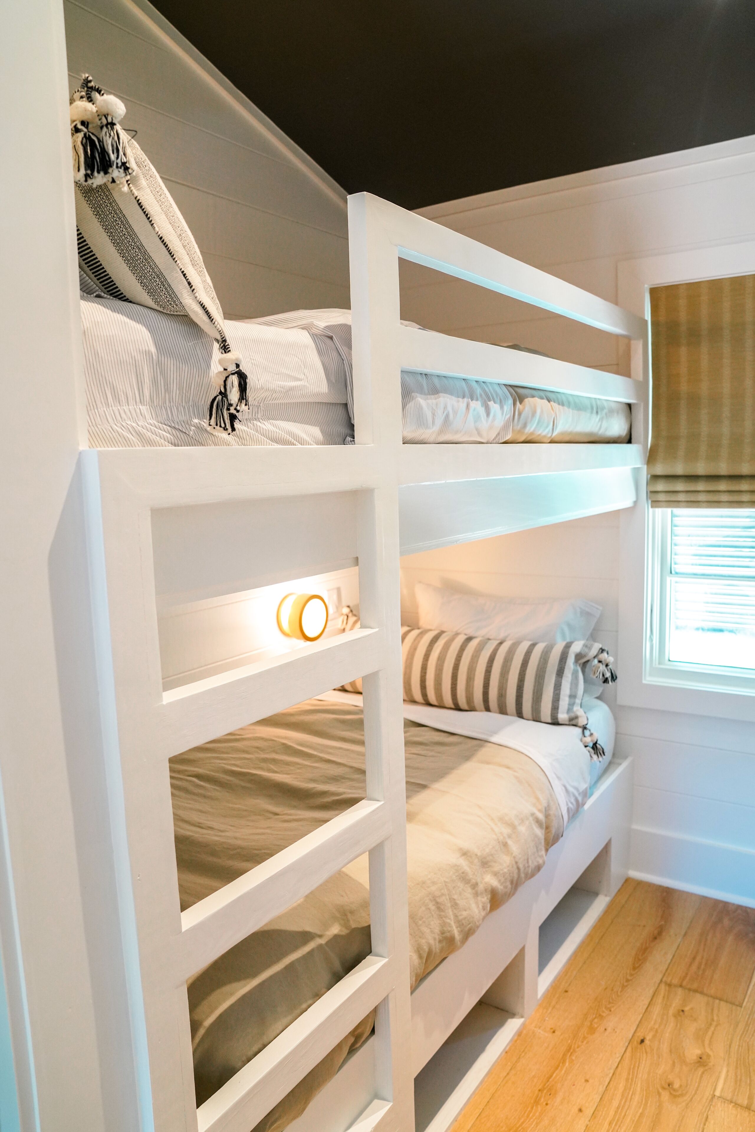 Een slaapkamer met een stapelbed, een raam, een bedlampje en een plank met een lamp.