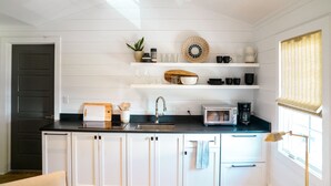 A modern kitchen with white cabinetry, a black countertop, a microwave, a coffee maker, and a window with a curtain.