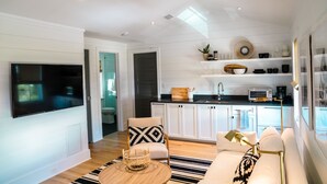 A modern living room with a flat-screen TV, a sofa, a coffee table, and a kitchen area with white cabinets and a microwave.