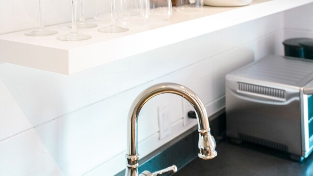 A kitchen with white cabinetry, a sink, and various kitchen items including a plant, a vase, and glassware.