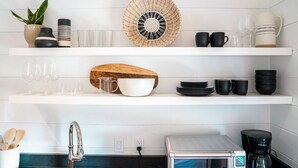 A kitchen with white shelves, a wooden cutting board, a coffee maker, and various kitchenware.