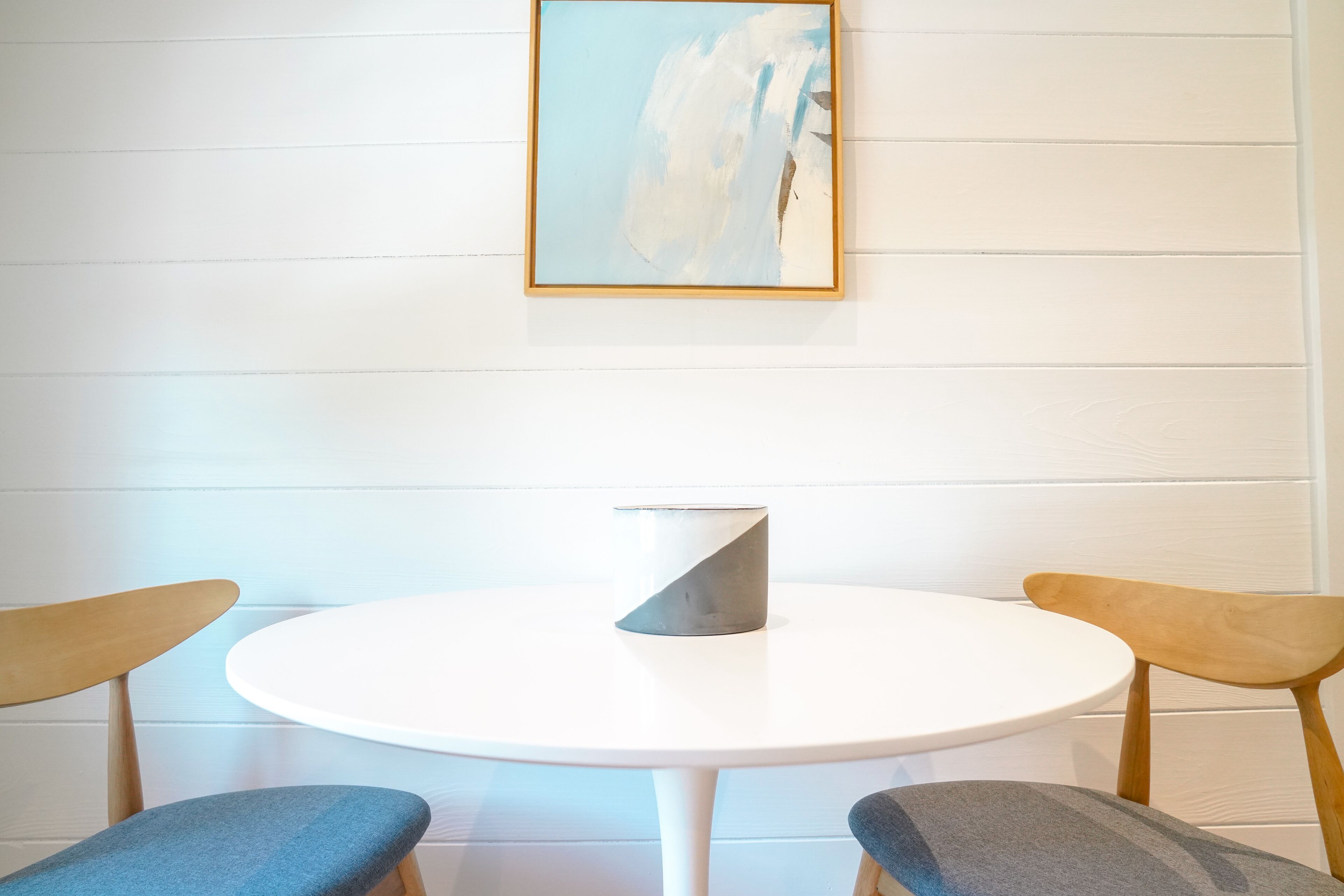 A round white table with a grey vase, flanked by two wooden chairs with blue cushions.