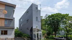 A modern two-story building with a grey facade, a small balcony, and a satellite dish. - Sakura (Kutchan)