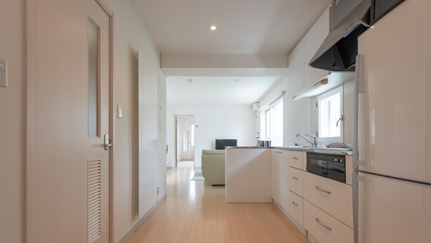 A modern kitchen with white cabinetry, a built-in oven, and a large window providing natural light. - Sakura (Kutchan)