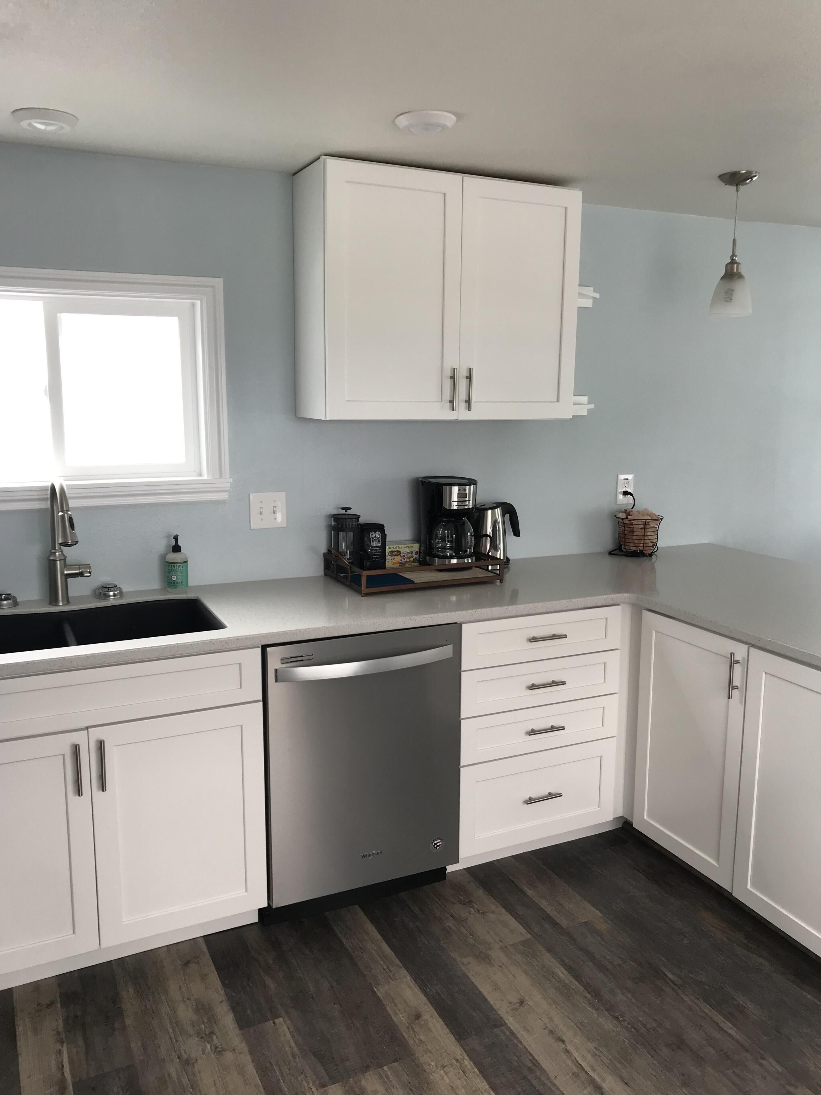 A modern kitchen with white cabinetry, a dishwasher, a coffee maker, and a window with natural light.