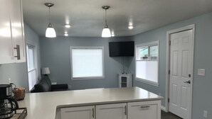 Een moderne keuken met witte kasten, een centraal eiland, hanglampen en een flatscreen televisie aan de muur.