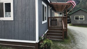 Een twee verdiepingen tellend huis met een veranda, een kleine tuin en een berg op de achtergrond.