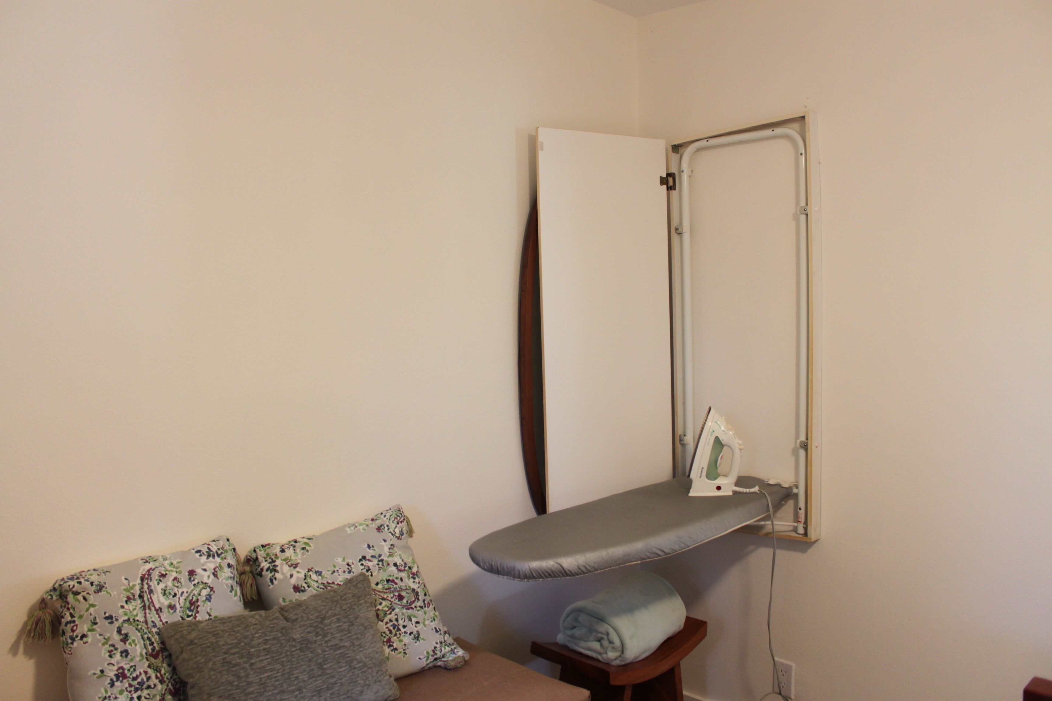 A room with a bed, an ironing board, and a mirror.