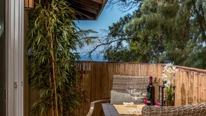 An outdoor seating area with a bamboo fence, wicker furniture, and a bottle of wine. - Reserve Your 5 STAR Big Island Get-a-way ⭐⭐⭐⭐⭐ (Waikoloa Village)