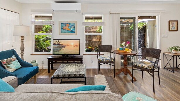 A living room with a TV, a sofa, a coffee table, and a dining area with chairs and a table. - Reserve Your 5 STAR Big Island Get-a-way ⭐⭐⭐⭐⭐ (Waikoloa Village)