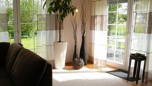 Una sala de estar con un sofá, un ventanal grande y dos plantas en macetas.