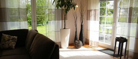 A living room with a sofa, a large window, and two potted plants.