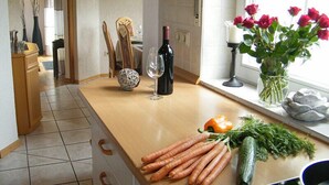 Una cocina con encimera de madera, una botella de vino, un jarrón con rosas y verduras frescas.