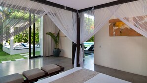 Une chambre moderne dotée d’un grand lit, d’un coin salon avec des bancs et offrant une vue sur l’extérieur grâce à de grandes fenêtres.