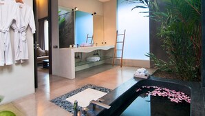 Une salle de bain moderne avec un grand miroir, une baignoire remplie de pétales de roses, une douche en verre et une plante en pot.