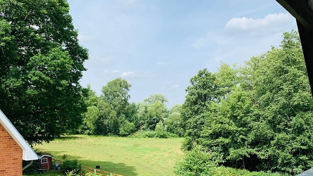 A view of a green field with trees and a brick building in the foreground.